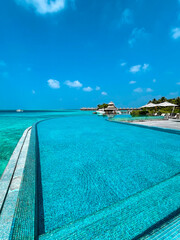 Scenic  landscape of Maldives beach and pier with speed boats and yachts on the horizon. Seascape with water bungalows, beautiful turquoise sea and lagoon waters, tropical nature paradise. 
