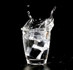 Ice cubes falling into the glass splashed by clear water