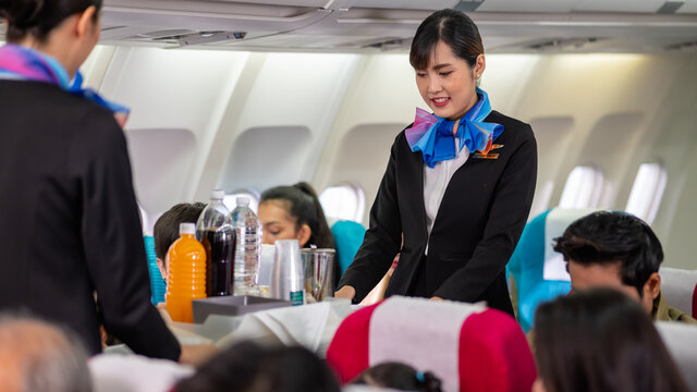 Two young beautiful Asian flight attendant serving food and drink to passengers on airplane. Two stewardess pushing food cart along aisle to serve the customer. Airline service business concept.