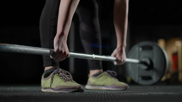 Anonymous female performs a deadlift with barbell, lifts barbell and does weights training in the gym, lower angle view.