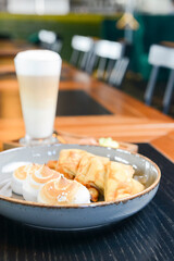Close up of french style sweet crepes with soft cream served with a tall glass of coffee latte on a wooden table.