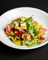 Vegetable salad with cheese, fresh romatoes and cucumbers, green olives served in a white plate over black background.