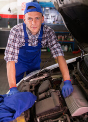 Professional mechanic man in uniform repairing car by customer claim order in auto repair shop garage