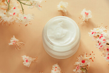 White cream jar and Horse chestnut flowers on beige background. Natural organic cosmetics concept. Top view