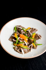 Buckwheat dumplings with fresh mushrooms served on a white plate over black background.