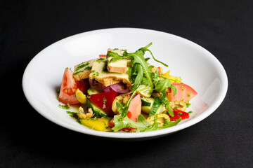 Vegetable salad with cheese, fresh romatoes and cucumbers, green olives served in a white plate over black background.