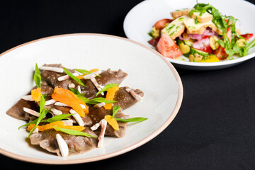 Buckwheat dumplings with fresh mushrooms and vegetable salad with cheese, fresh romatoes and cucumbers over black