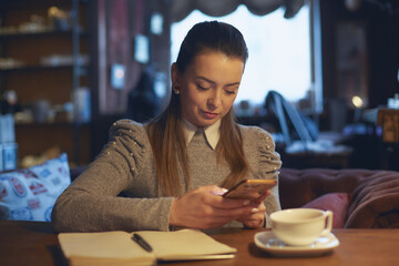 Beautiful woman sitting in a cafe at a table drinking tea and making notes in a notebook
