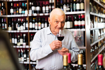 Older man customer holding glass of wine before buy it in a wine house. High quality photo