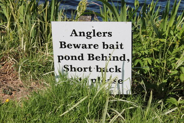 Anglers beware bait pond behind. Back casts please. sign partially obscured by grass