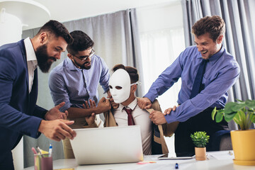 Male colleagues in office, sitting at table together, sharing ideas, discussing project strategy. Businessman hidden behind the mask