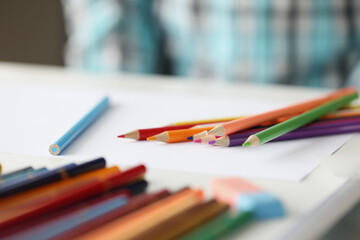 Many multi-colored pencils lying on blank sheet of paper closeup
