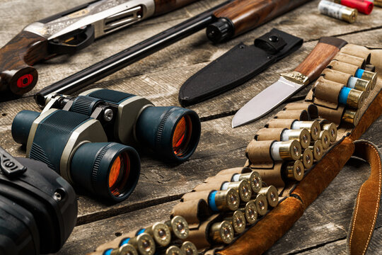 Hunting equipment on old wooden background including rifle, knife, binoculars and cartridges