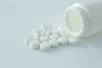 On a white background lies a plastic bottle with pills scattered nearby