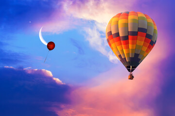 Hot air balloon flying in colorful evening sky with new moon shining. Only single red helium balloon flies up into the sky