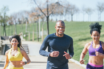 Two women and a man with a mask running in a park.