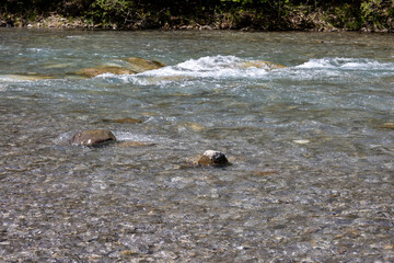 Wunderschöner Gebirgsfluss in den Alpen mit Panorama und kleinen Wasserfällen