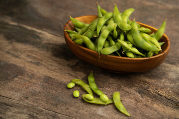 edamame beans in wooden bowl on textured wooden table.