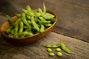 edamame beans in wooden bowl on textured wooden table.