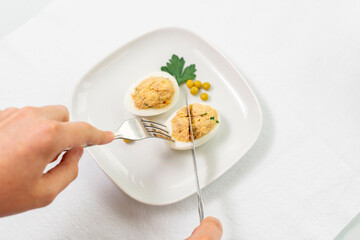 stuffed eggs with canned tuna and herbs. man cuts off a piece of egg