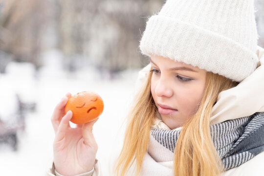 young beautiful woman is sad in winter. holding a tangerine in his hand with a painted sad face. the girl is lonely.
