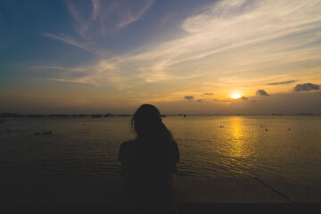 Back view silhouette young girl asian with depressed pose on the beach at sunset. Beautiful blonde woman with long hair depressing at the ocean. Concept of depress, sad