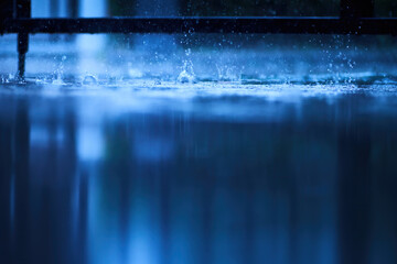 a blue scene of wet reflection floor from heavy raining with splashing water from rain droplet, photograph shot with very shallow depth of field focusing