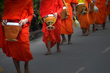 Buddhist monks walking barefooted during the traditional morning alms or Sai Bat in Luang Prabang,...