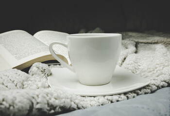 Cup of hot tea and a book on white bed blanket.