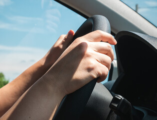 Female hands on the steering wheel of a car while driving.