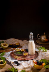 Dark moody food photography of a passion fruit smoothie bottle with blackberries. Natural and healthy drink concept.