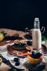 Dark moody food photography of a passion fruit smoothie bottle with blackberries. Natural and healthy drink concept.