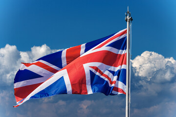 Union Jack Flag. Close-up of a national UK flag with flagpole, blowing in the wind on a blue sky with clouds and copy space.
