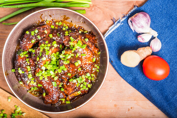 Pieces of pork and pork ribs cooked in a spicy sauce on a plate on the table and ingredients nearby on a denim napkin