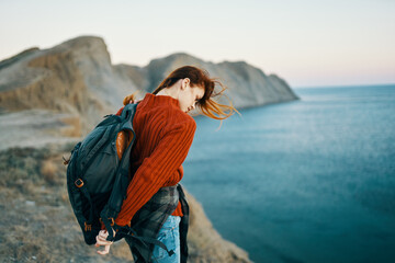 woman in a sweater with a backpack walks in nature in the mountains near the sea