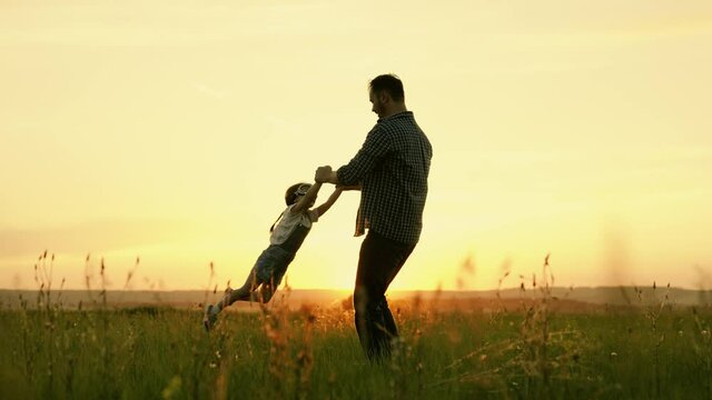 Happy family, dad plays with child as pilot, circling child by hands, kid rejoices and laughs. Silhouette of father and child, little girls, playing, enjoying sunset in park in nature on summer day.