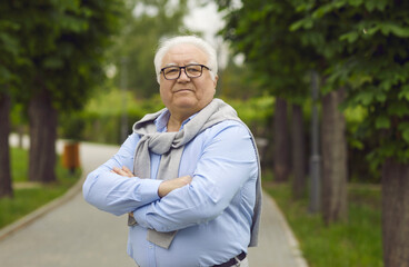 Portrait of confident senior citizen. Elderly man in glasses and shirt standing on park pathway and...