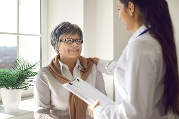 Beautiful mature woman sitting in medical office, looking at doctor and listening to advice with...