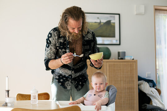 Man holding bowl and feeding baby son