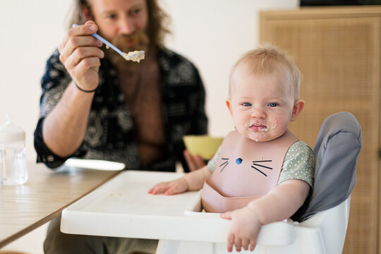 Man feeding baby son sitting in high chair