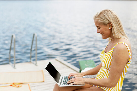 Woman in swimsuit using laptop at lake