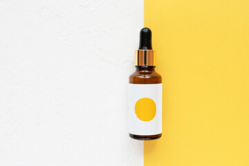 Beautiful brown glass skincare bottle on a white and yellow background, flat lay.
