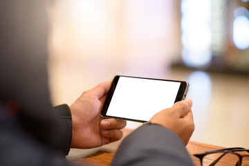Mockup image of a man holding and using mobile phone with blank white desktop screen with on the table