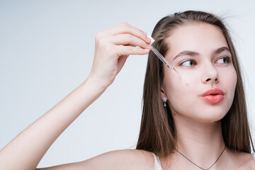 An attractive young girl gets rid of imperfections by applying serum on her face with a pipette in her hand