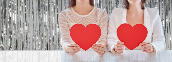 homosexuality, valentine's day and love concept - close up of happy lesbian couple holding red paper hearts over foil party curtain on background