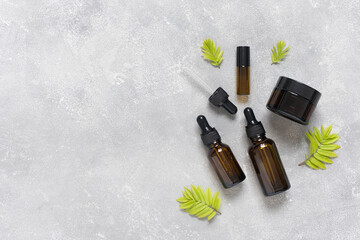 Bottles of dark amber glass with essential oil and face cream on a gray concrete background. SPA...