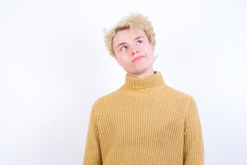 Young handsome Caucasian blond man standing against white background has worried face looking up...