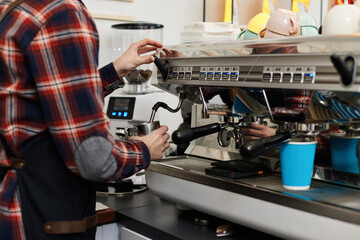 barista in apron pours fresh coffee into a cup