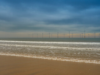 Fototapeta na wymiar The near-shore wind farm at Redcar, with waves breaking on the beach sands in the foreground, the wind farm on the horizon and a deeply coloured sky.