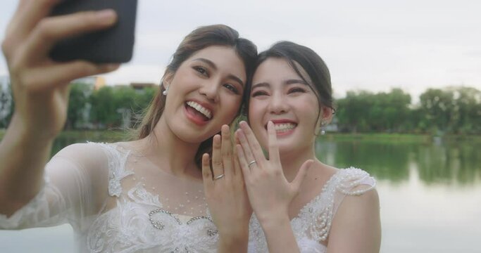 Happy Asian Lesbian Married Couple On Wedding Day. The Married Couple Happily Chatting Over Video Calls With Friends.